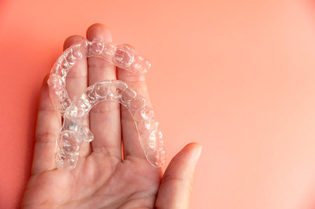 Female palm of Caucasian woman holding transparent polymer dental aligners on color background for teeth alignment. Aesthetic and comfortable teeth alignmentの写真素材