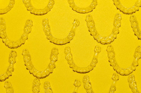 Clear dental aligners on colored yellow background, close-up side view from above. Pattern of clear bracesの写真素材