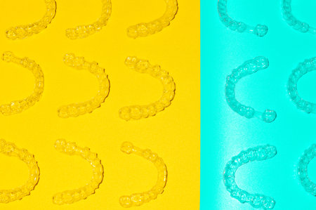Invisible orthodontic cosmetic aligners on a colored background, aligners, plastic braces. Modern dental retainers created on a 3D printerの写真素材