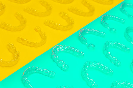 Invisible orthodontic cosmetic aligners on a colored background, aligners, plastic braces. Modern dental retainers created on a 3D printerの写真素材