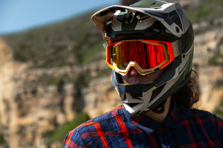 Close-up portrait of young sportsman wearing protective helmet and protective mask on his face. Mature guy resting looking at camera after hard training in mountainsの写真素材