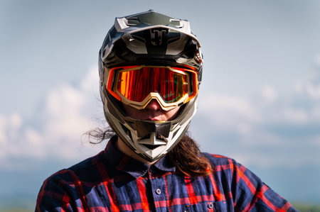 Close-up portrait of young sportsman wearing protective helmet and protective mask on his face. Mature guy resting looking at camera after hard training in mountainsの写真素材