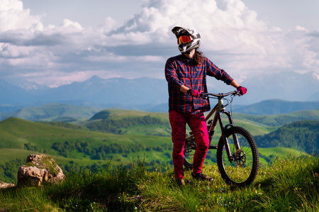 Athlete rider in bicycle helmet on his bike standing and resting before descent in mountains against the backdrop of epic mountains and landscape. MTB downhill discipline background.の写真素材