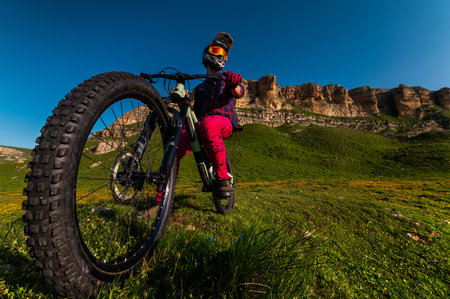 Rider cyclist man wearing mask and full face helmet standing on his bike on top of hill high in mountains. Space copy background for mountain bikingの写真素材