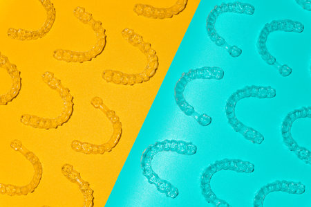 Transparent dental aligners on light blue and yellow background, close-up. Top view of pattern laid out from plastic braces for alignment. Background for advertising dental servicesの写真素材