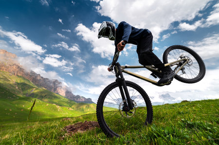 professional man in a full-face helmet performs a front wheelie trick in a field in the mountains in summer. An unrecognizable sportsman shows a manual trickの写真素材