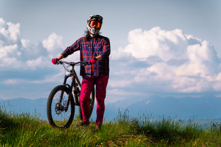 Unrecognizable athlete in protective gear standing in a field and looking at the camera against the backdrop of foggy mountains and cumulus clouds. Mountain sports conceptの写真素材