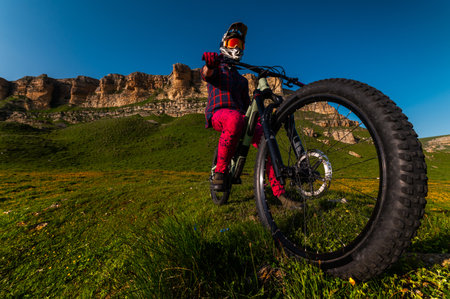 Wide angle shot of a downhill mountain bike wheel in the foreground, with the athlete sitting confidently on the bike. Sharp rocky mountains are visible in the backgroundの写真素材