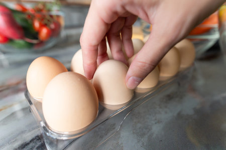 Human hand with eggs takes or puts one clean egg on the background of kitchen table with prepared ingredients. Food preparation conceptの写真素材