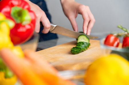 woman manually cuts a fresh cucumber, preparing it for cooking in a salad. chopping vegetables. Homemade healthy food conceptの写真素材
