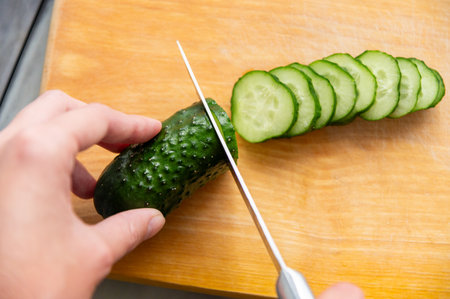 Top view from first person on a knife cutting a fresh green cucumber into rings. Female hands preparing a saladの写真素材