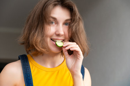 Portrait of a girl happily biting a piece of sliced cucumber. Healthy eating or diet to lose weight and slim down for the summerの写真素材