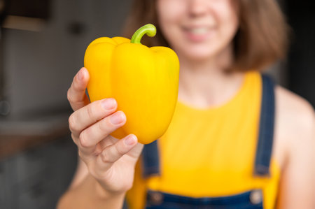 Yellow pepper in a female hand against the background of a smiling girl, close-up of a healthy vegetableの写真素材