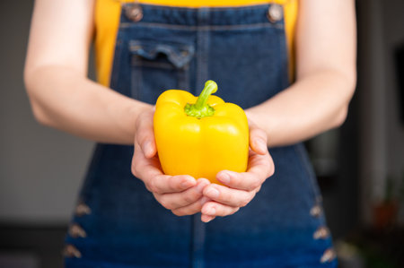 Unrecognizable woman holding yellow bell pepper standing in kitchen. Close up of hands, person following healthy lifestyle, veganism, vegetarianismの写真素材