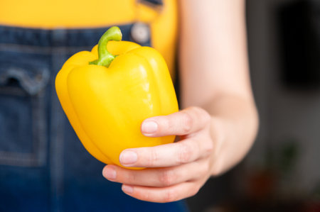 Close-up of yellow bell pepper in unrecognizable female hand. Girl hands pepper, sense of movementの写真素材