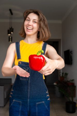 Cheerful happy girl gets into the camera bell pepper and points at it, calling to eat. Healthy eating conceptの写真素材