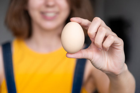One chicken egg is held in a womans hand. Concept of demonstrating sizes. Chicken egg. Hand holds a chicken egg. Girls hand shows an egg on the background of itselfの写真素材