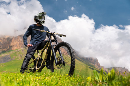 Cyclist standing with bicycle in fresh air. Tourist relaxing in field with hills view enjoying beautiful mountain landscape wearing helmet covering whole face. Active recreation conceptの写真素材