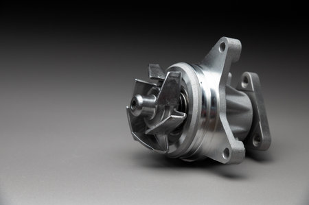 A new, shiny aluminum engine coolant pump on a gray gradient background. Contrast backlighting.