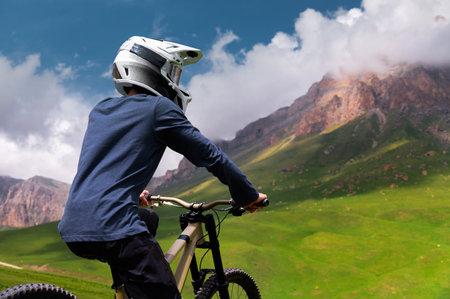 Man sits on a bicycle in a green field with mountains in the background. Concept of mountain biking and outdoor trainingの写真素材