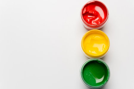 Green, yellow, and red gouache jars on a white background. Plastic paint jars for childrens crafts without lids. Materials for drawing, creativity, and early childhood developmentの写真素材