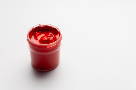 A jar of red colored gouache on a white background. Copy space. A transparent jar of colored water-soluble paint.の写真素材