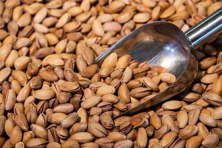 A large number of unshelled pistachios are on the store shelf. A stainless steel scoop is immersed...
