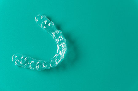 Clear dental aligner placed on a solid turquoise background, showcasing its transparent design and...