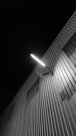 Street photography of outdoor wall lamp brighten up over the metal sheet wall of construction site...