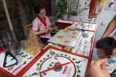 Jul 20, 2017 - Chengdu, China: Sugar candy art made by a woman behind bar in Jinli Pedestrian Street in Chengdu. A boy chooses design by spinning wheel and get a candy art in 10 yuan.のeditorial素材