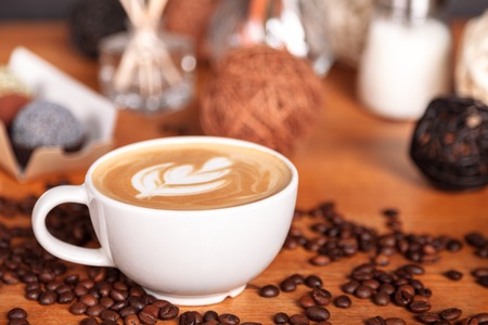 Close-up of a Cup of latte or cappuccino with latte art. Coffee and cakes on a wooden table with scattered coffee beans. The concept of the presentation of coffee in coffee shopsの写真素材