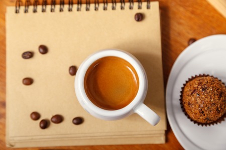 A Cup of espresso with foam and a notebook, scattered coffee beans on a wooden table. Coffee break conceptの写真素材