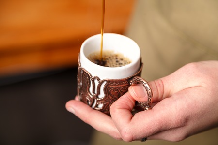 Barista pours Turkish coffee into a traditional embossed metal copper Cup, close-up, selective focusの写真素材