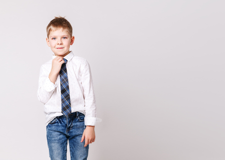 Cute little smiling boy in white shirt and in a stylish tie posing on a light-gray background. Portrait of fashionable male child, gray wall on background. Concept of children style and fashionの写真素材
