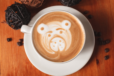 White Cup cappuccino coffee with a latte-art pattern in the form of a bear close-up on a wooden background. The concept of making coffee in a coffee shopの写真素材