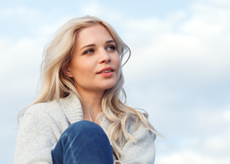 Beautiful happy blonde in a gray sweater and jeans smiling against the blue sky. Travel, leisure,...