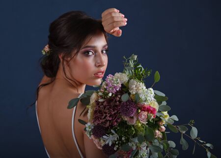 Bridal bouquet and hairstyle. Bouquet of the bride in hand, the bride turns her back with a bouquet in her hand, against the blue wallの写真素材