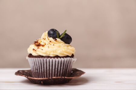 Delicious cupcake with whipped cream and chocolate on a blurred background of beige wall. Concept of advertising confectionery productsの写真素材