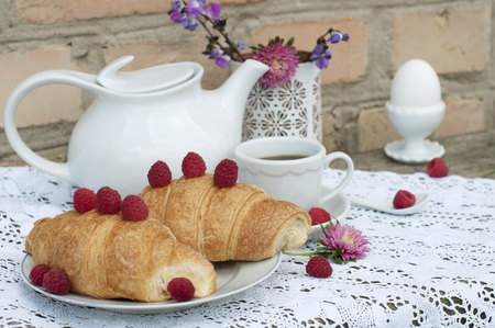 Breakfast with cup of coffee. A dessert with croissants and berries of raspberry on white a lace tableclothの写真素材