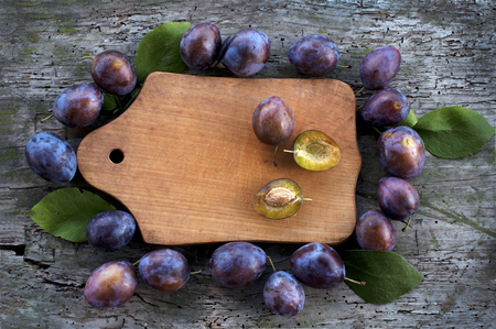 Ripe plums around a wooden board on a wooden backgroundの写真素材