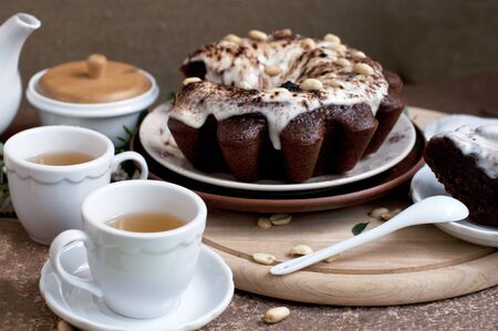 Chocolate cake with peanuts on table with tea and flowersの写真素材
