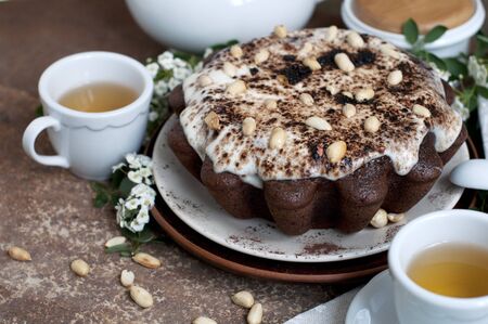 Chocolate cake with peanuts on table with tea and flowersの写真素材