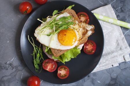 Sandwich with fried egg, meat, tomato and salad. Breakfast on a black plate. Top viewの写真素材