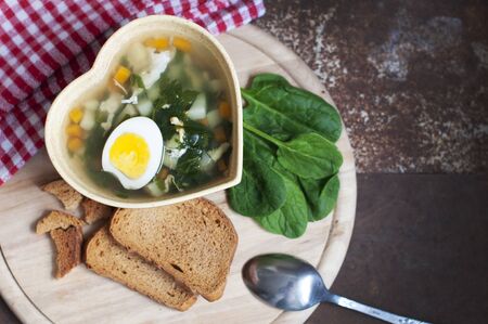 Green borsch with sorrel, parsley, egg and grens in the bowl form of heart with spoon on wooden background. Top viewの写真素材