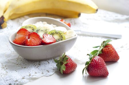 Breakfast with oatmeal with strawberries, kiwi and banana on white background. Breakfast for child. Oatmeal in a white heart-shaped plateの写真素材