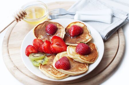 Breakfast with pancakes with strawberry, kiwi and honey. Breakfast for child on wooden backgroundの写真素材