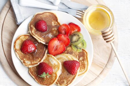 Breakfast with pancakes with strawberry, kiwi and honey. Breakfast for child on wooden background. Top viewの写真素材
