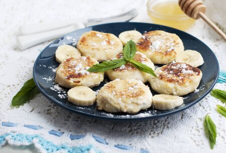 Cottage cheese pancakes, syrniki with banana and mint in blue plateの写真素材