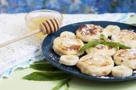 Cottage cheese pancakes, syrniki with banana and mint in blue plateの写真素材