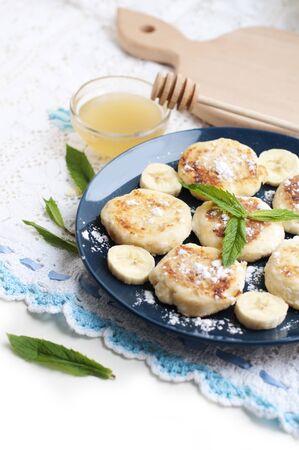 Cottage cheese pancakes, syrniki with banana and mint in blue plateの写真素材